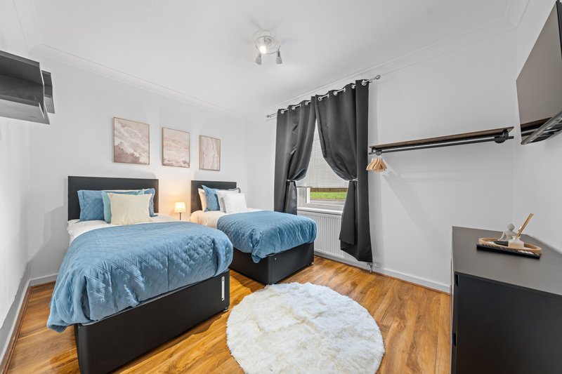 Bedroom with two single beds, blue quilts, wooden floor and grey curtains