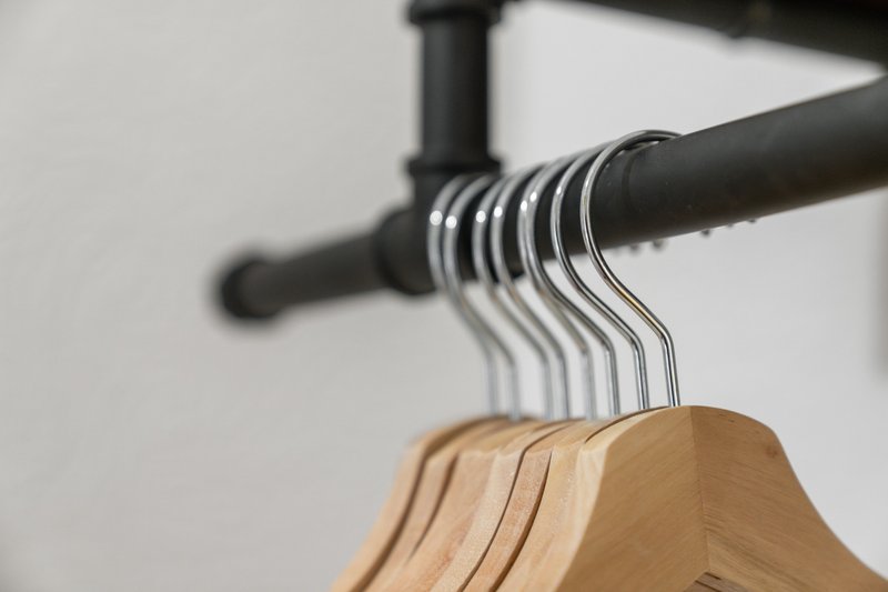 Wooden clothes hangers on metal rod with industrial pipe fixtures