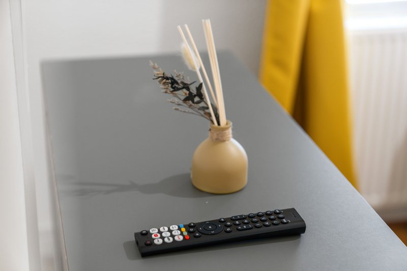White shelf with cream diffuser, dried flowers, remote control and yellow curtain