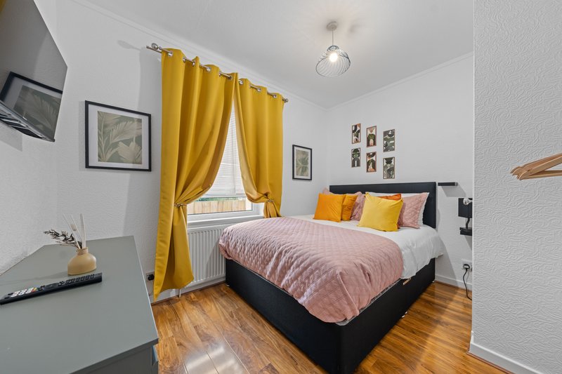 Bedroom with double bed, yellow curtains, wooden floor and wall art