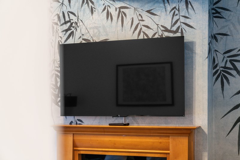 Living room wall with flat-screen TV mounted above wooden cabinet and decorative foliage wallpaper