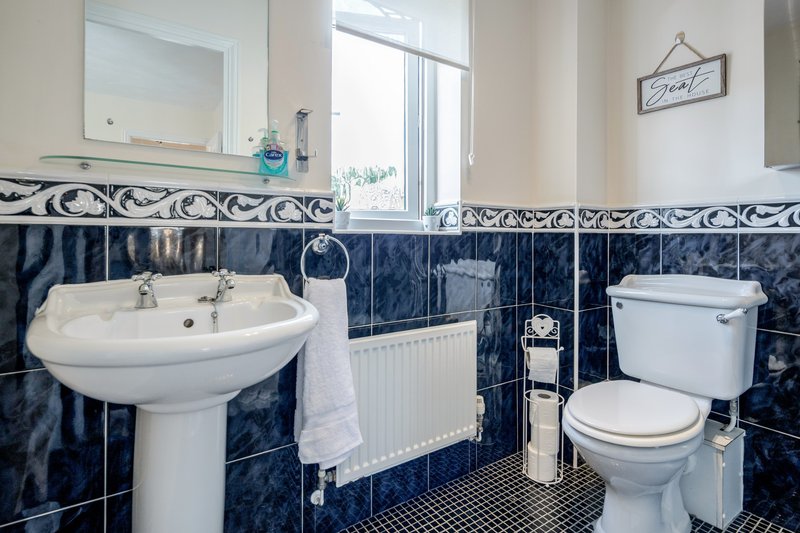 Bathroom with pedestal sink, toilet, radiator, and blue tile walls with decorative border