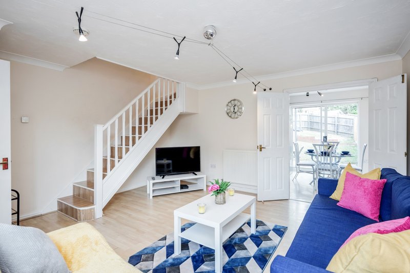 Bright open-plan living room with blue sofa, white staircase, TV, and wooden flooring
