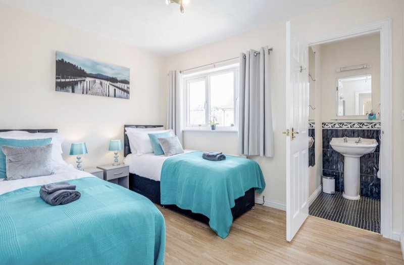 Bright bedroom with two single beds, turquoise bedding, and ensuite bathroom visible through open door