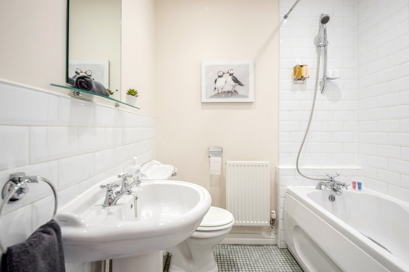 Bright bathroom with pedestal sink, toilet, bathtub with shower, white subway tile walls and framed wall art