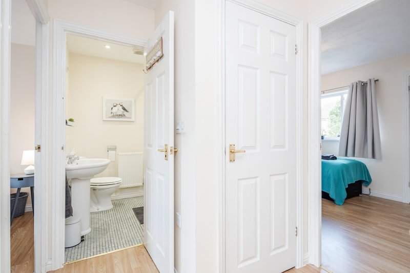 Hallway with open bathroom door showing toilet and sink, bedroom doorway with teal bedding visible