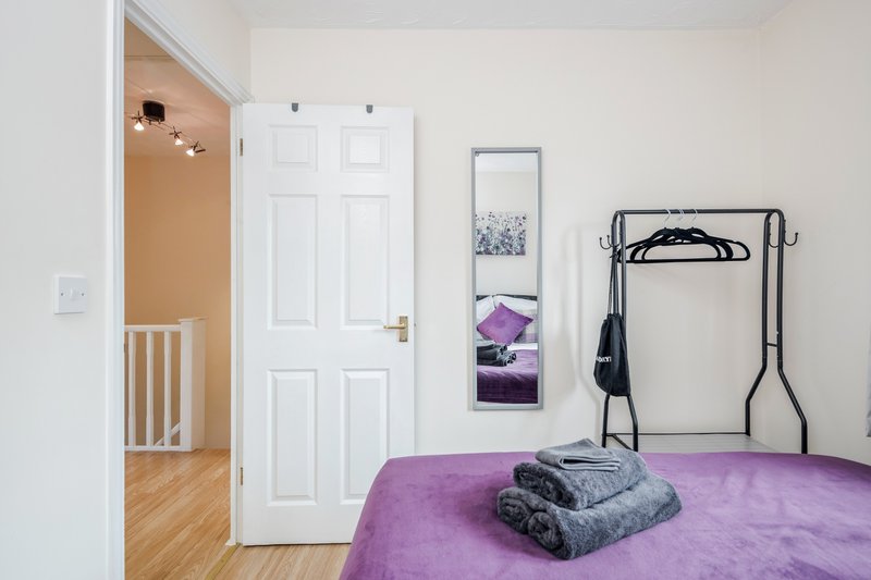Bedroom with purple bedding, folded towels, white wardrobe, and exercise equipment rack.