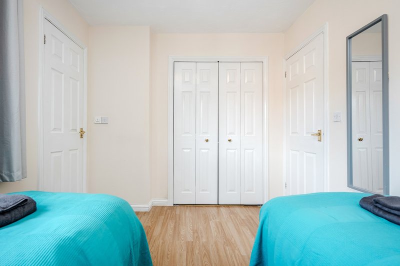 Twin bedroom with two turquoise beds, wooden floor, white wardrobes and doors