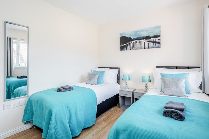 Bright twin bedroom with turquoise bedding, white walls, wooden floor and landscape artwork