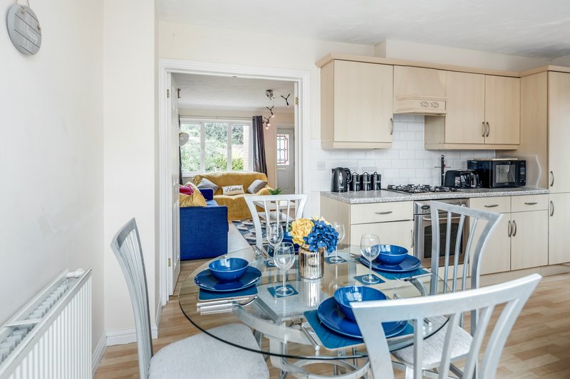 Open-plan kitchen and dining area with glass table, blue place settings and wooden cabinets