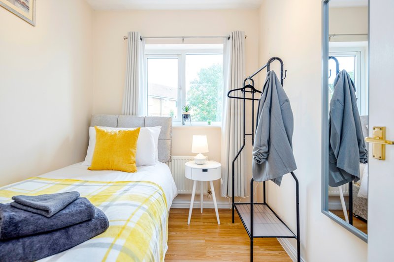 Bright bedroom with single bed, yellow bedding, towels on rack and mirror door