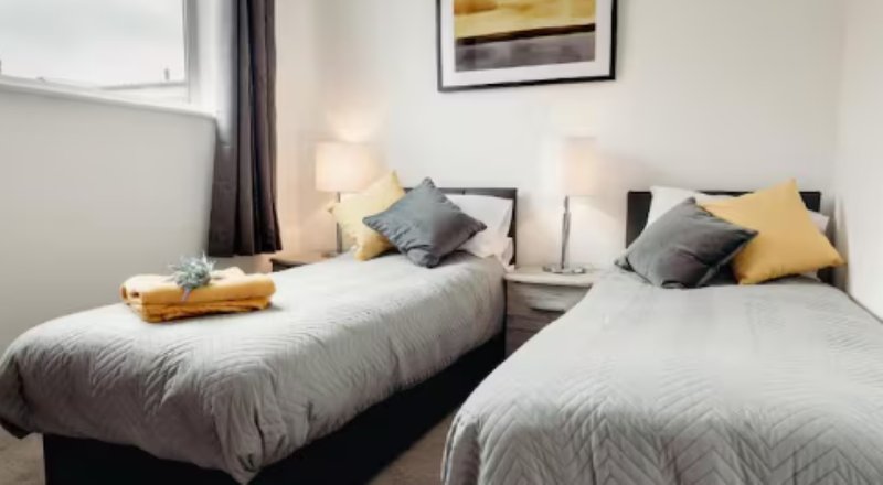 Twin bedroom with two single beds, grey bedding, yellow cushions, and bedside lamps