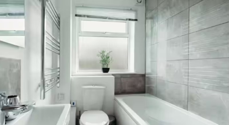 Modern bathroom with toilet, bathtub, heated towel rail and window with plant