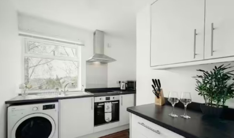 Modern kitchen with white cabinets, black countertops, integrated appliances and window
