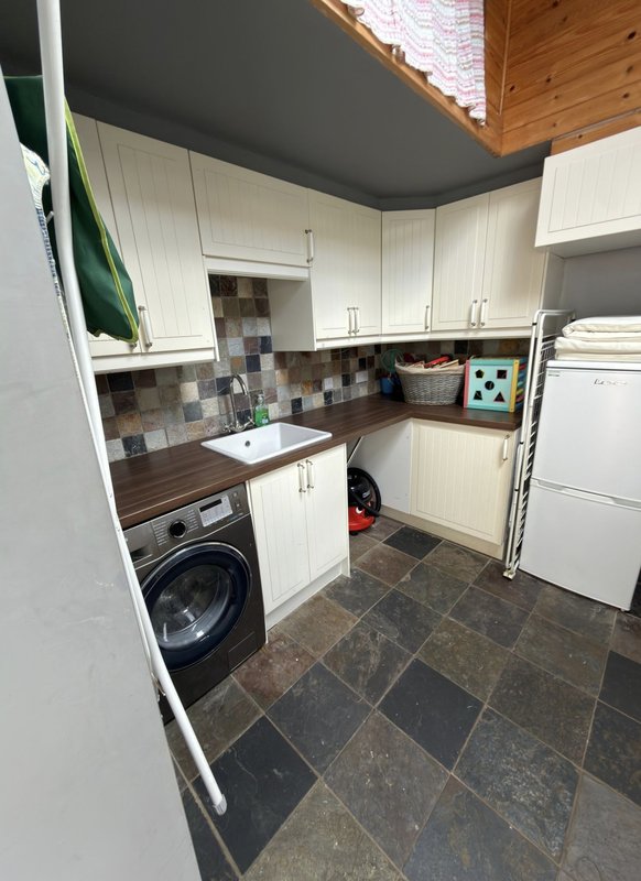 Compact laundry room with washer, sink, white cabinetry, and tile flooring