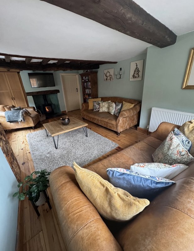 Spacious open-plan living room with exposed beams, brown leather sofa, fireplace and wooden flooring