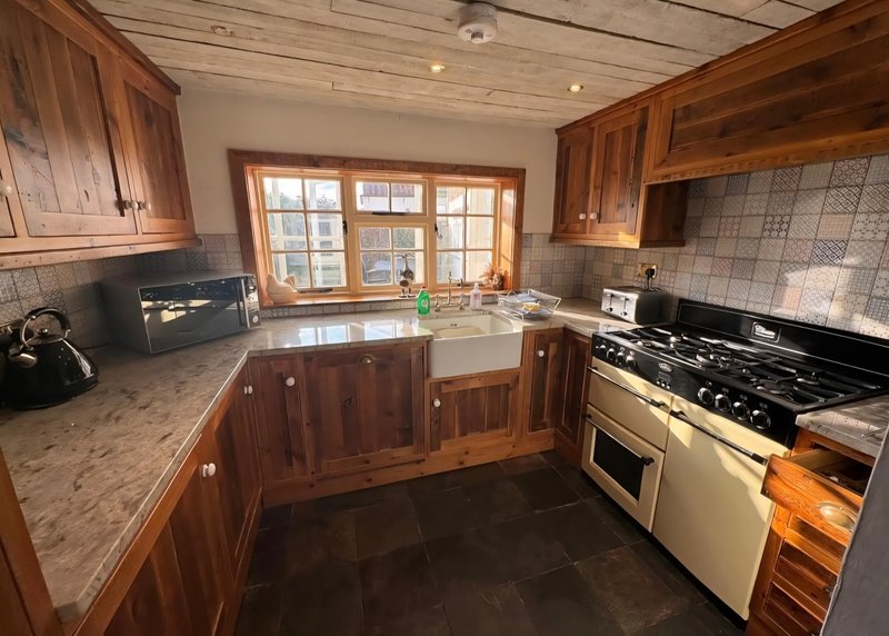 Kitchen with wooden cabinets, cream Aga cooker, marble countertop and window.
