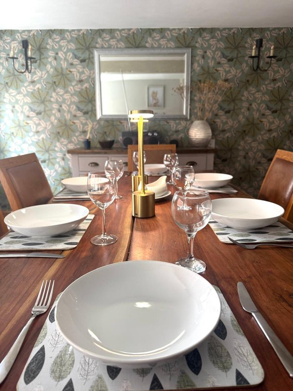 Formal dining room with wooden table, place settings, wine bottle, and patterned wallpaper