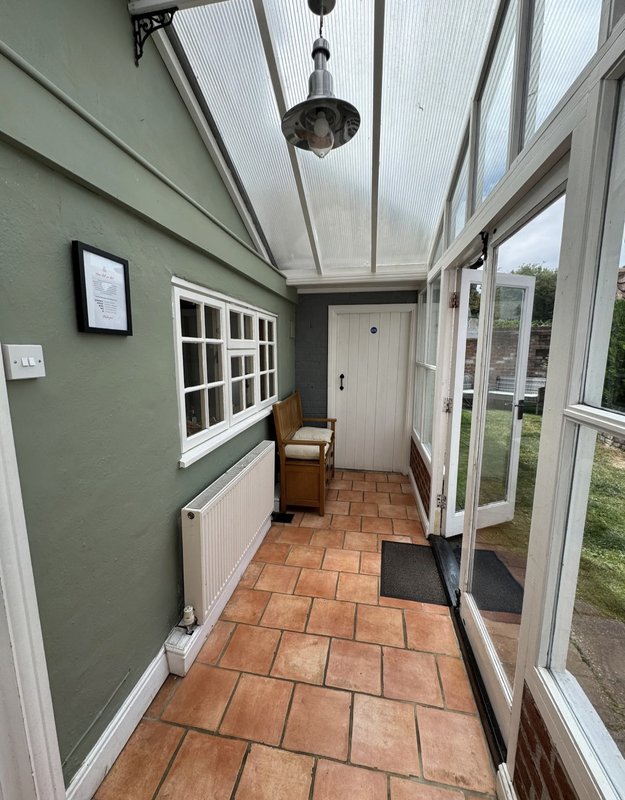 Bright conservatory with green walls, terracotta tile floor, white door and windows