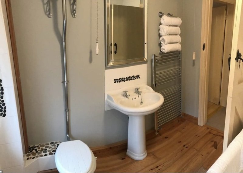 Bathroom with pedestal sink, mirror, towel rack, toilet and wooden flooring