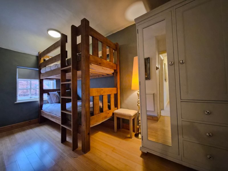 Bedroom with wooden bunk bed, wardrobe, small stool, and hardwood flooring