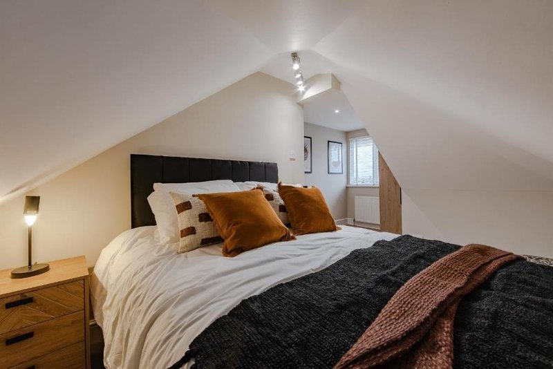 Attic bedroom with double bed, wooden headboard, ochre cushions and bedside lamp