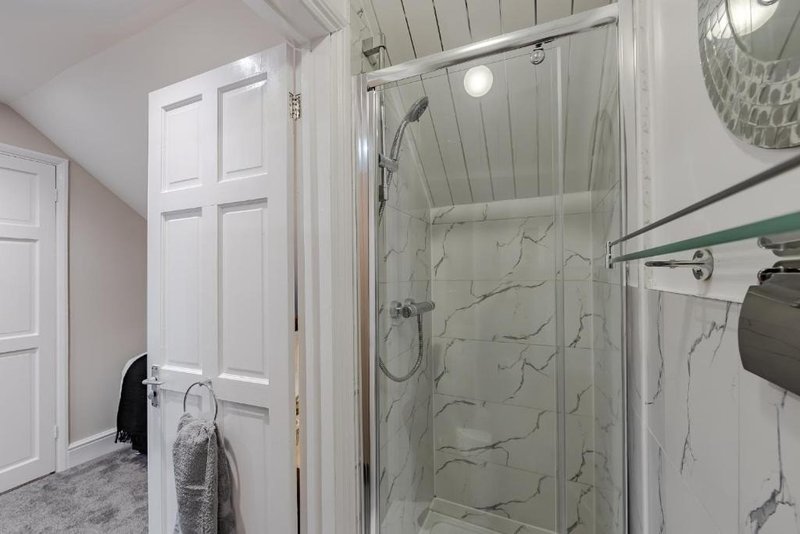Bathroom with walk-in shower, marble walls, towel rack and white cabinetry