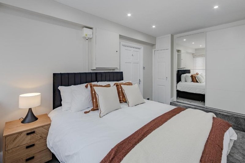 Modern bedroom with double bed, black headboard, wooden nightstand and mirror wardrobe