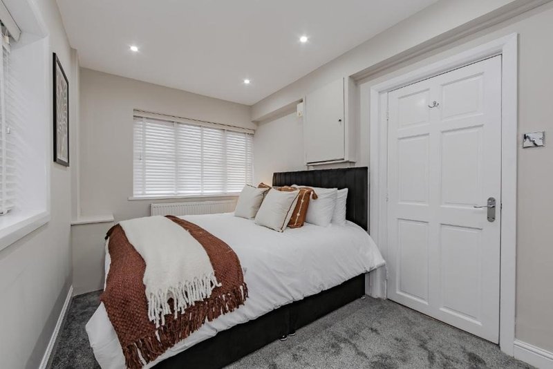 Bedroom with black bed, white bedding, brown throw, window with blinds and white door