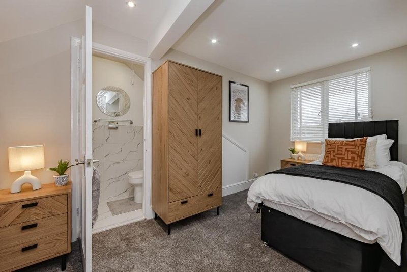 Modern bedroom with black bed, wooden wardrobe, ensuite bathroom, and bedside lamp