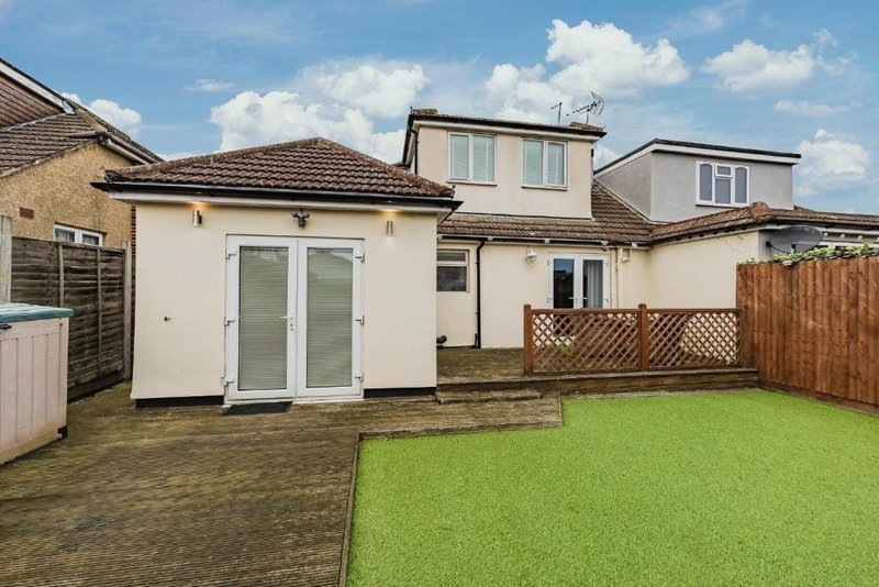 Modern house exterior with extended rear section, paved patio area and manicured lawn garden