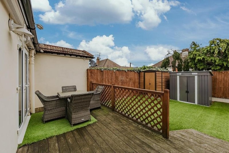 Backyard garden with decking, artificial grass, wicker seating and wooden fencing