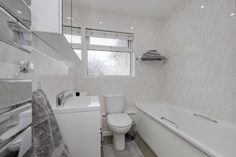 Modern bathroom with white suite, bath, sink, toilet, and gray towel hanging on rail