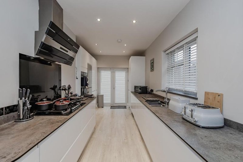 Modern galley kitchen with white cabinetry, granite countertops, stainless steel appliances and pendant lighting