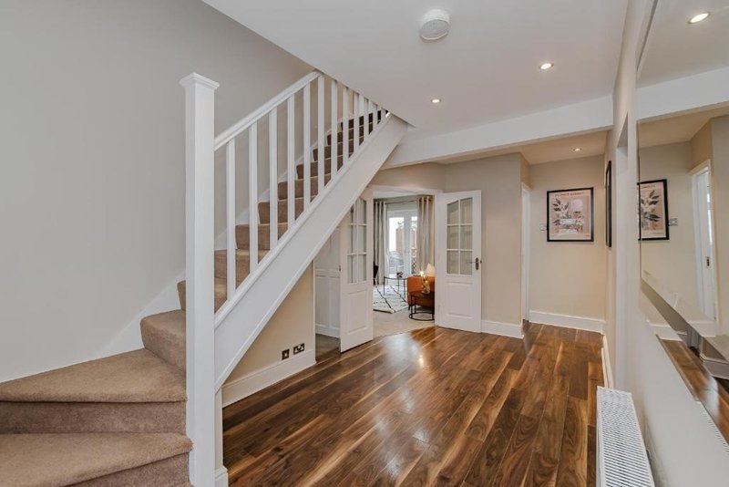 Bright hallway with wooden staircase, hardwood flooring, white walls and doors leading to other rooms