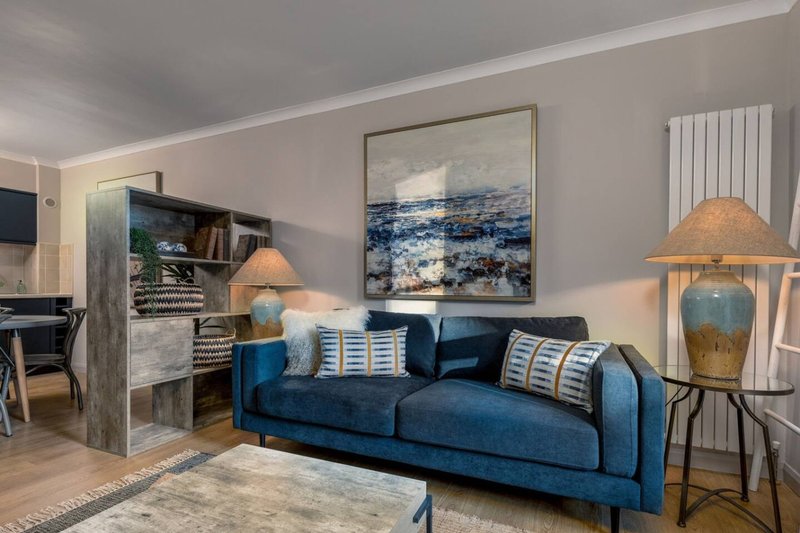 Modern living room with blue sofa, coastal artwork, table lamps and wooden furniture