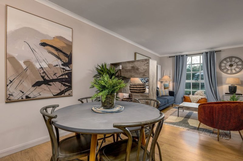 Open-plan dining and living room with round table, chairs, artwork, and modern furnishings