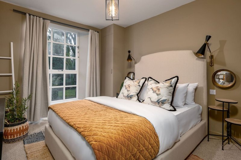 Modern bedroom with queen bed, gold bedspread, patterned pillows, and large window with curtains