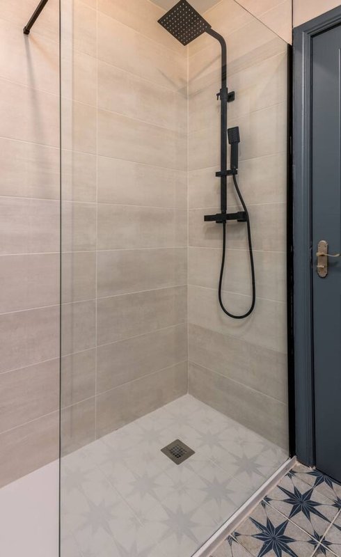 Modern bathroom shower enclosure with black fixtures, neutral tile walls and floor