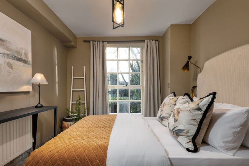 Bedroom with double bed, yellow throw, white bedding, desk, lamp and large window with countryside view