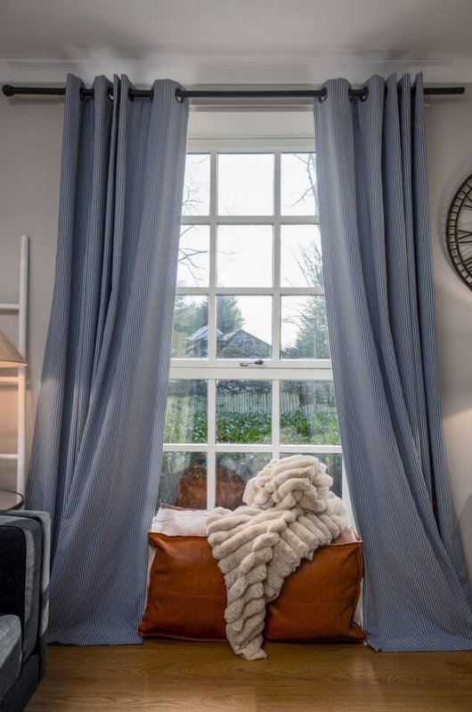 Bedroom window with blue curtains, cushions and cream throw blanket on windowsill
