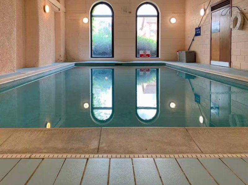 Indoor swimming pool with arched windows, wooden decking, and wall-mounted lighting