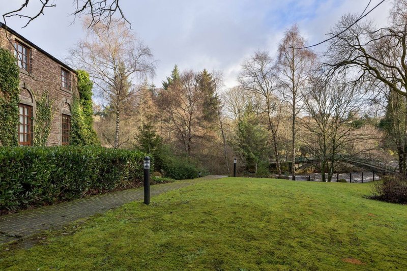 Stone building with ivy-covered wall, large open lawn and mature trees in grounds