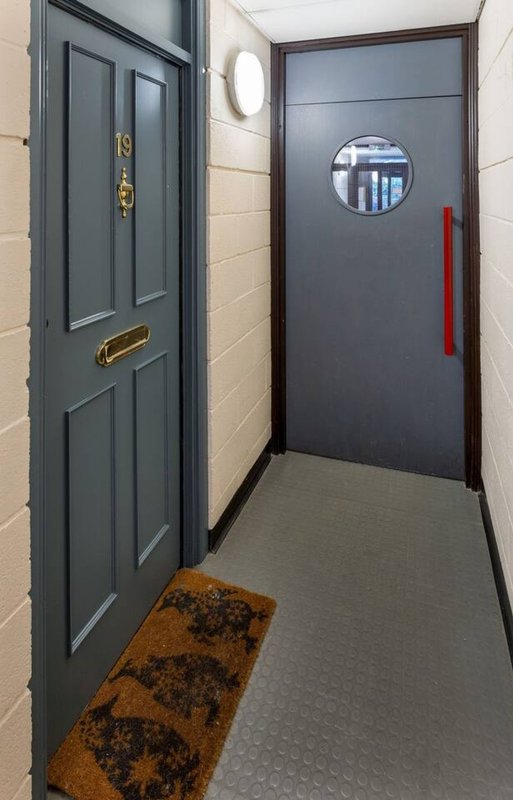 Hallway with two dark doors, round window, brown doormat and gray flooring
