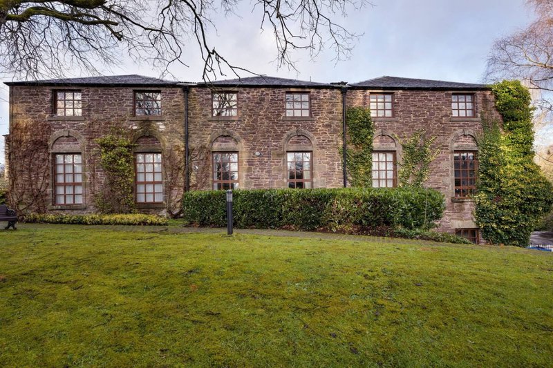 Stone-built property exterior with ivy, manicured lawn, multiple windows and bare tree branches