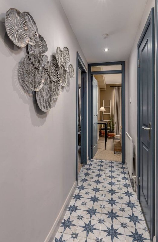 Narrow hallway with geometric patterned floor, white walls, decorative woven plates, and blue doors