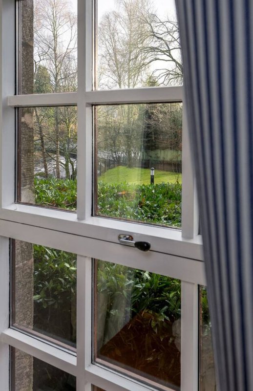 Window with grey curtains overlooking garden with bare trees and green lawn