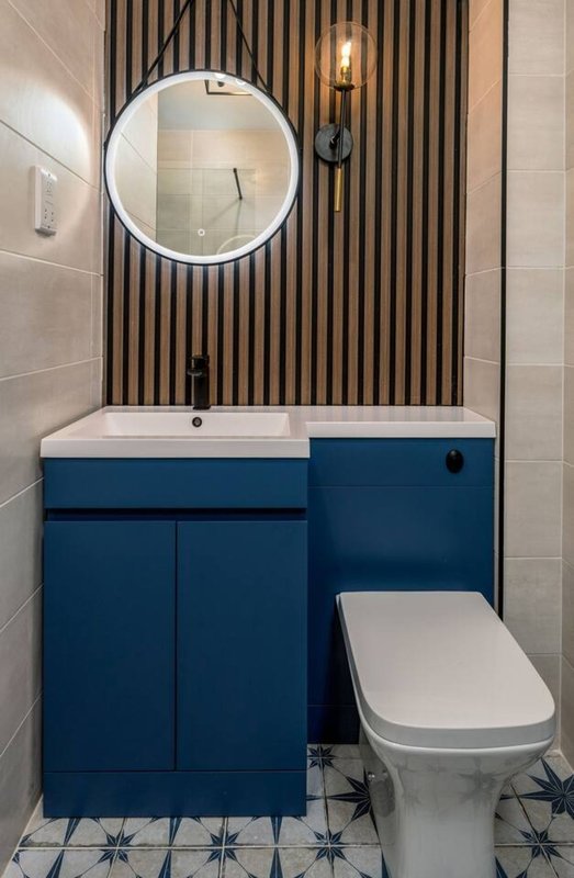Modern bathroom with blue vanity, round mirror, wall sconce and toilet
