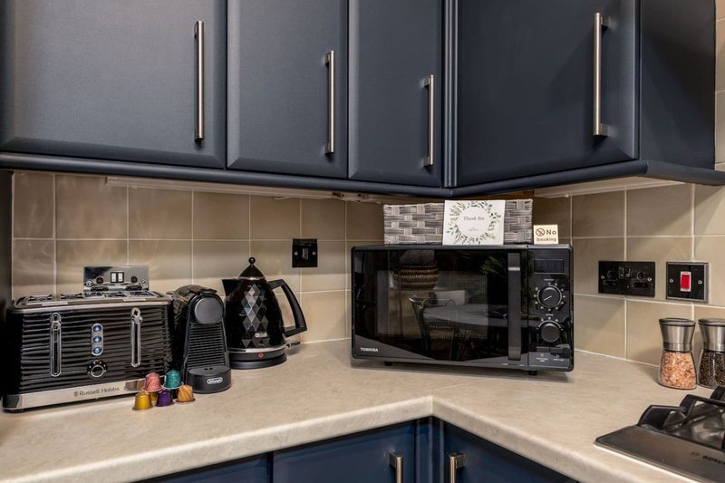 Modern kitchen with dark blue cabinetry, beige tile backsplash, and countertop appliances