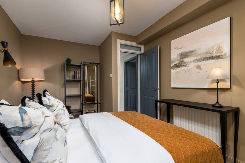 Bedroom with double bed, wooden bedding bench, artwork, and navy blue wardrobe doors